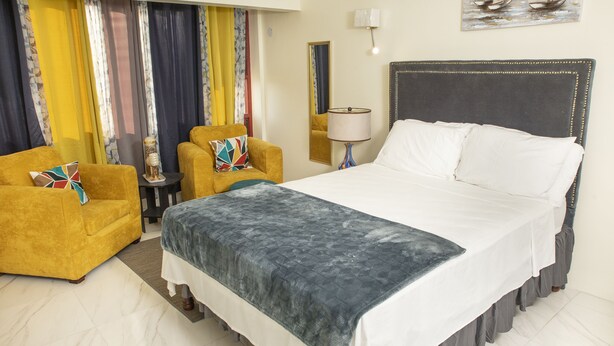Una habitación de hotel con una cama grande, dos sillones, una mesita y una lámpara.
