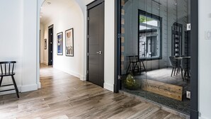 Un intérieur moderne avec un plancher en bois, une porte d’entrée en verre et un coin repas visible à travers la vitre.