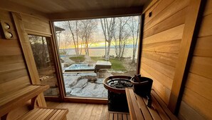 Un sauna en bois, avec des bancs et un jacuzzi visible à travers la porte en verre.