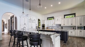 Une cuisine moderne avec des meubles blancs, un grand îlot central doté de tabourets et une vue sur l’extérieur par une fenêtre.