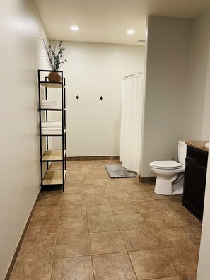 Une salle de bain avec des toilettes, une étagère avec des serviettes pliées, un rideau de douche et une plante en pot.