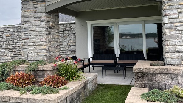 A house with a stone exterior, a covered patio with outdoor furniture, and a view of a lake. - Luxury Lakeside/Trailside Living (Hancock)