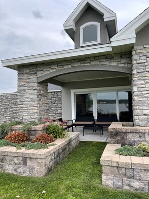 A house with a stone exterior, a covered patio with outdoor furniture, and a view of a lake. - Luxury Lakeside/Trailside Living (Hancock)