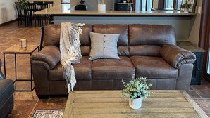 A spacious living room with a leather sofa, a wooden coffee table, and a kitchen in the background. - Luxury Lakeside/Trailside Living (Hancock)