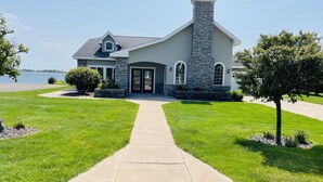 A modern two-story house with a stone chimney, a front door, and a driveway leading to the entrance. - Luxury Lakeside/Trailside Living (Hancock)