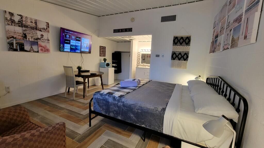 A bedroom with a bed, a chair, a desk, and a television on the wall.