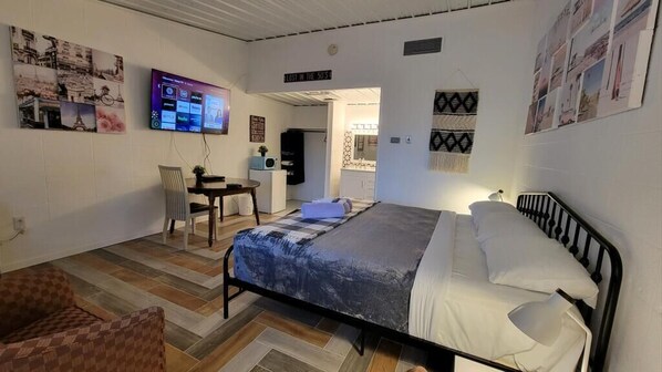 A bedroom with a bed, a chair, a desk, and a television on the wall.