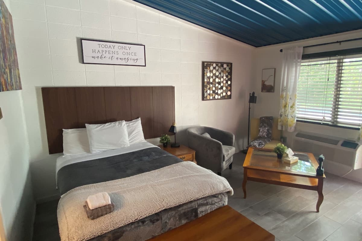 A neatly arranged bedroom with a bed, a chair, a small table, and a decorative sign on the wall.