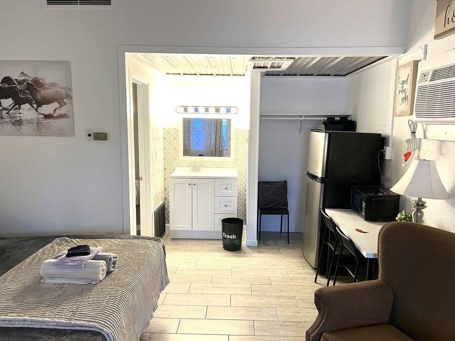 Un dormitorio con cama, una silla, un escritorio con computadora y televisor.