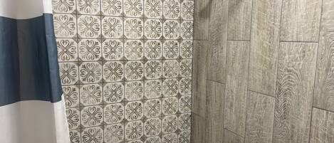 Zona de ducha con azulejos estampados, un cabezal de ducha metálico y una bañera.