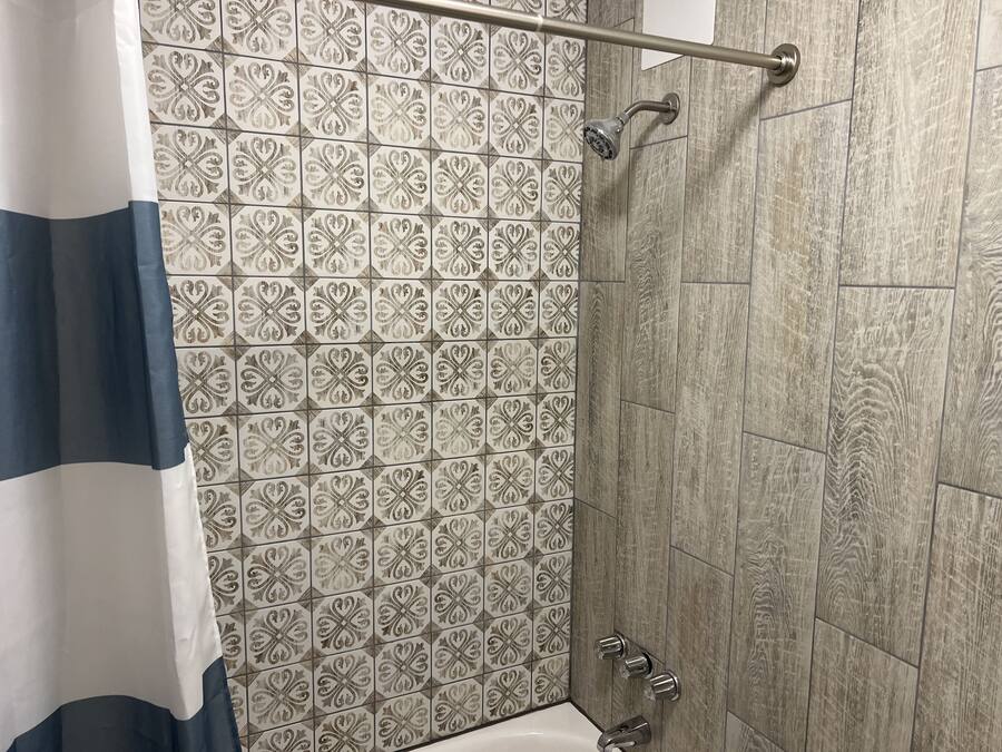 Zona de ducha con azulejos estampados, un cabezal de ducha metálico y una bañera.