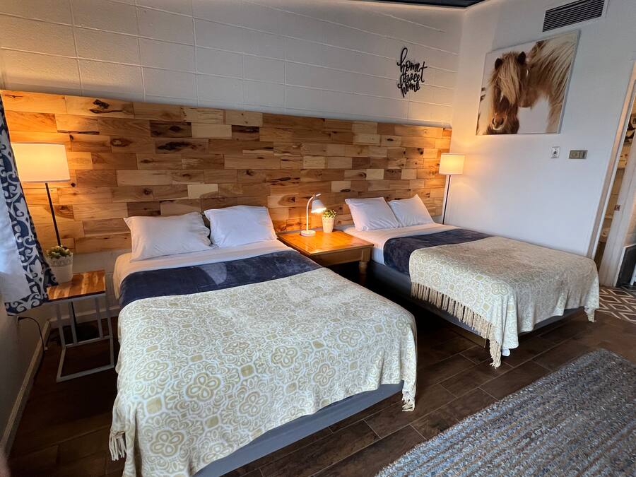 Une chambre d’hôtel avec deux lits, une tête de lit en bois, des lampes de chevet, une petite table et une œuvre d’art accrochée au mur.