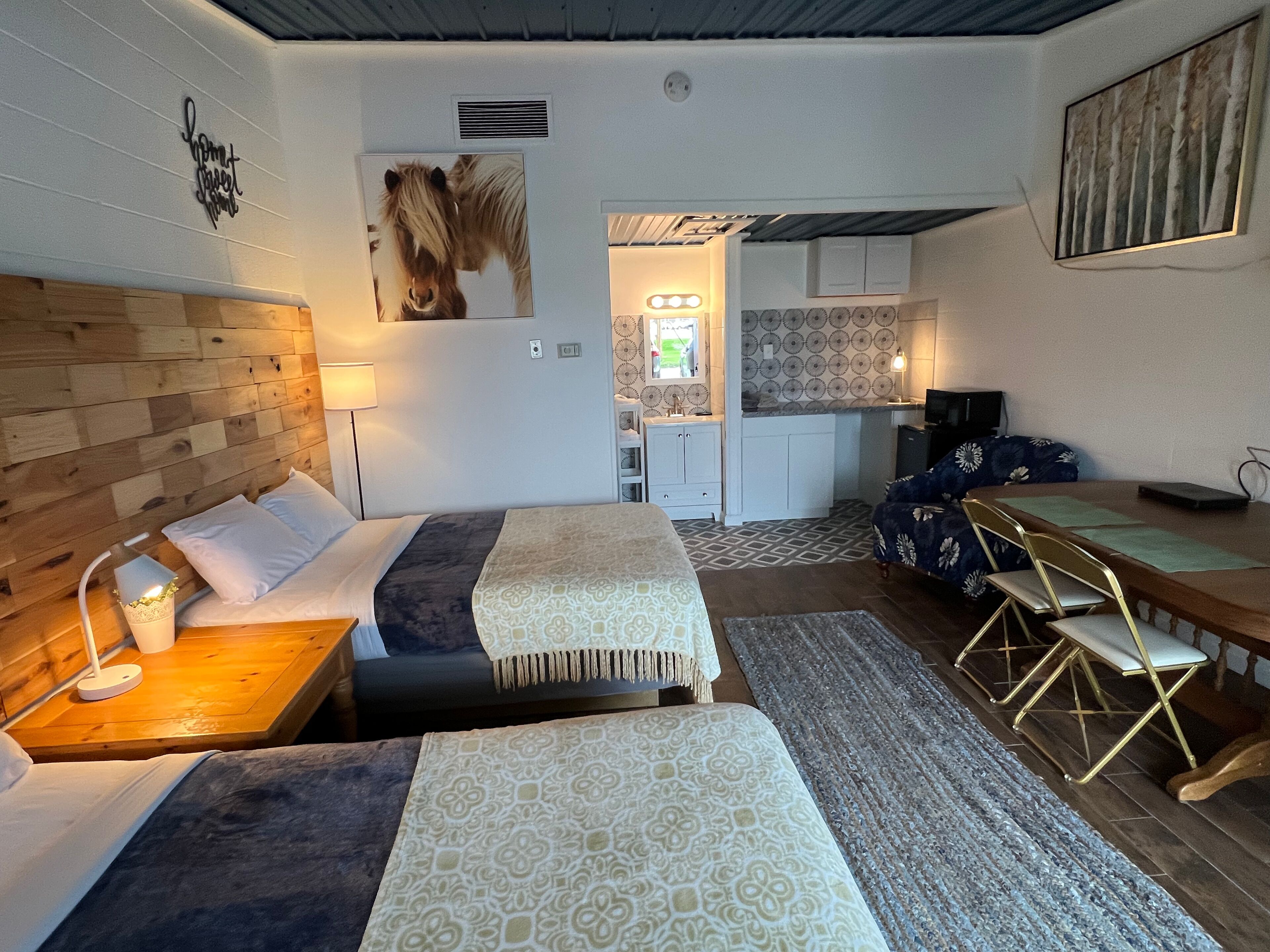 A hotel room with two beds, a small kitchenette, a dining table, and a TV.