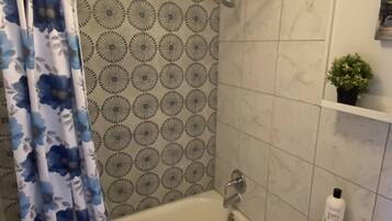 A bathroom with a bathtub, shower curtain, toilet, and a small potted plant on the wall.