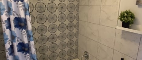 Een badkamer met een bad, douchegordijn, toilet en een kleine plant in een pot aan de muur.