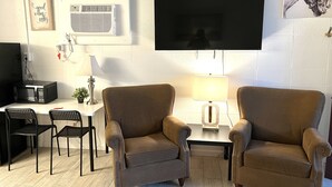 Olohuoneessa on kaksi nojatuolia, sohvapöytä, taulutelevisio, mikroaaltouuni sekä pieni pöytä, jossa on lamppu.