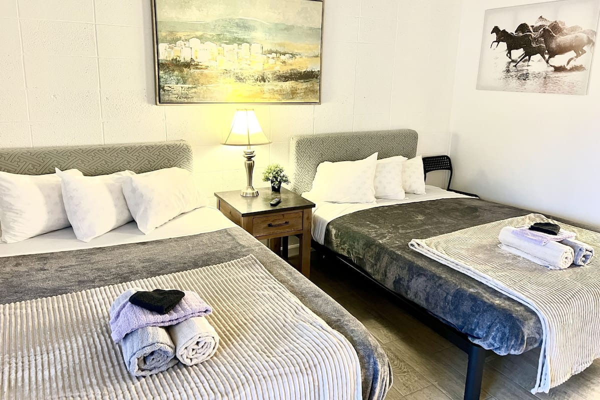 A hotel room with two beds, a nightstand with a lamp, a painting on the wall, and a towel rack.