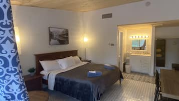 Un dormitorio con cama, mesita de noche, lámpara y un baño con lavabo y espejo.