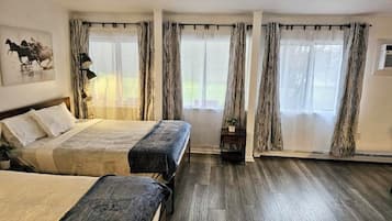 A bedroom with two beds, a large window with curtains, a lamp, and a painting on the wall.