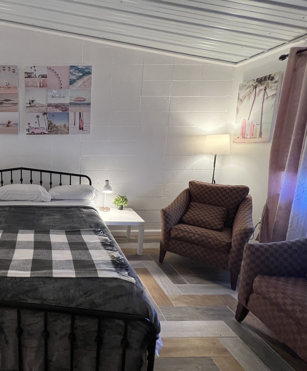 A bedroom with a bed, a chair, a small table with a lamp, and a wall with pictures.