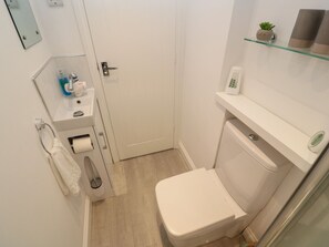 A compact bathroom with a toilet, sink, and a small shelf with a plant.