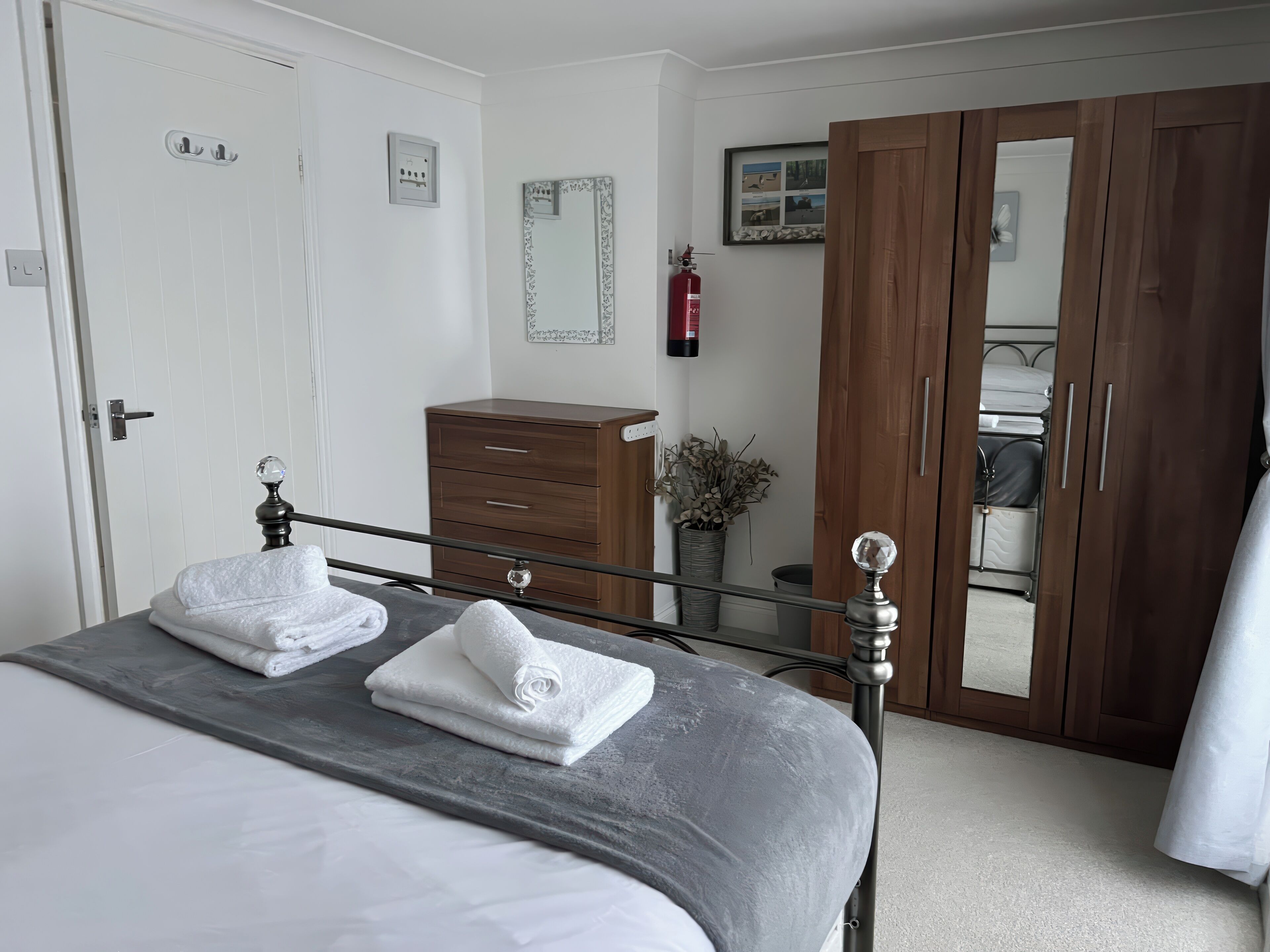A neatly made bed with white towels, a wooden dresser, a mirror, and a wardrobe.