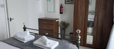 A neatly made bed with white towels, a wooden dresser, a mirror, and a wardrobe.