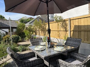 An outdoor patio with wicker furniture, a table set for dining, and a large umbrella providing shade.