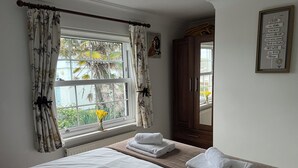 Un dormitorio con cama, ventana con cortinas, mesita de noche con toallas, armario y una cita motivacional en la pared.