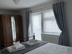 A bedroom with a bed, a wardrobe, a window with curtains, and a radiator.