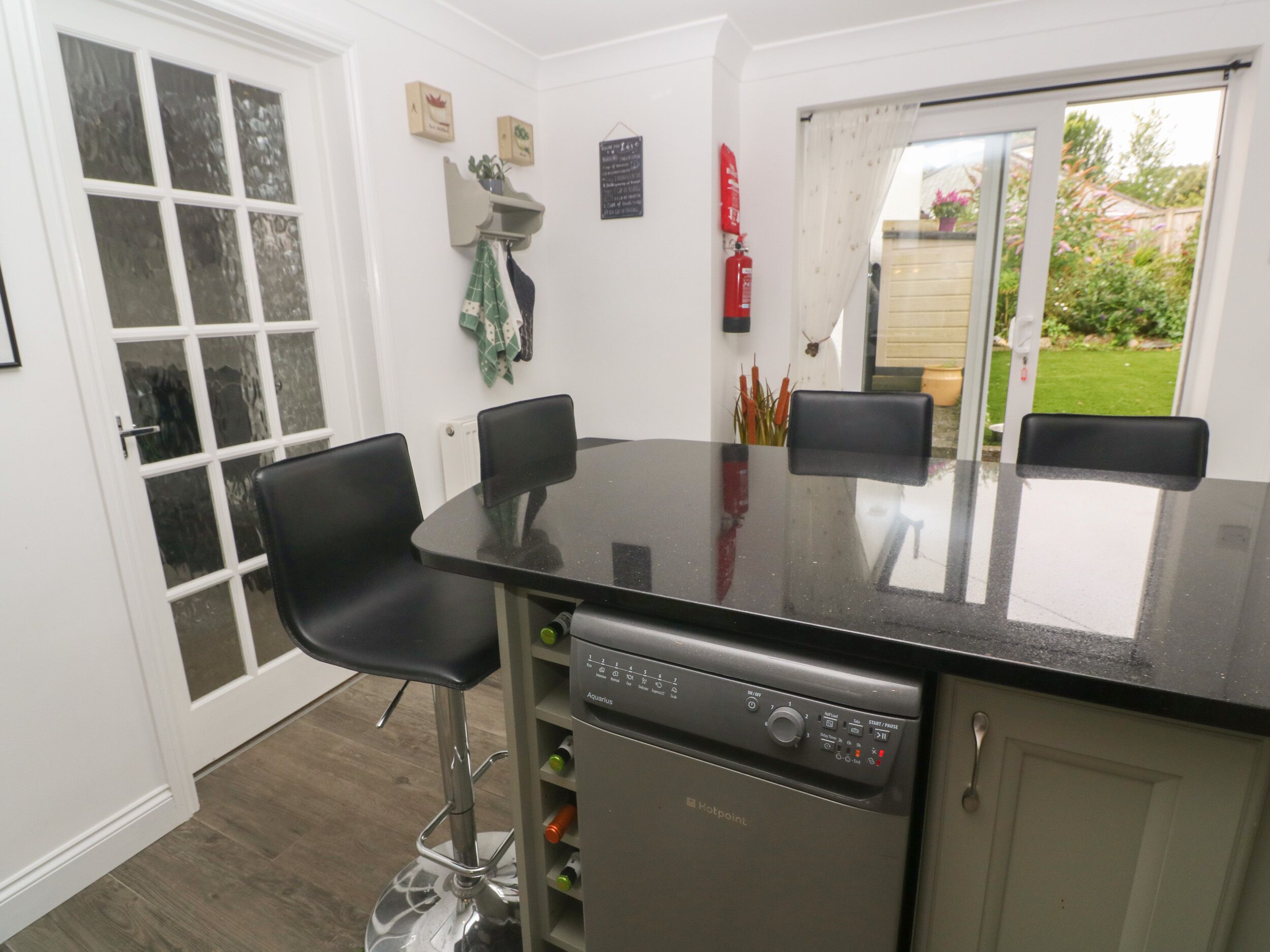 A kitchen with a black countertop, two black chairs, a dishwasher, and a window with a view of a garden.