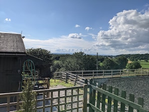 A rural landscape with a wooden building, a fenced area, and a view of distant hills. - Rustic Log Cabin - Dog Friendly - Sleeps 2 - Views (Shrewsbury)