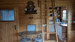 A wooden cabin interior with a dining table, chairs, a ladder, shelves, a clock, and a framed quote on the wall. - Rustic Log Cabin - Dog Friendly - Sleeps 2 - Views (Shrewsbury)