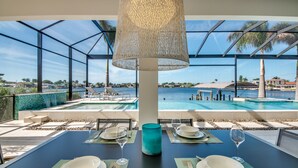 Comedor con una mesa dispuesta para dos, con vista a una piscina y un paisaje.