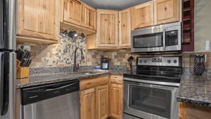 Una cocina con armarios de madera y electrodomésticos de acero inoxidable, incluyendo un refrigerador, lavavajillas, microondas y horno.