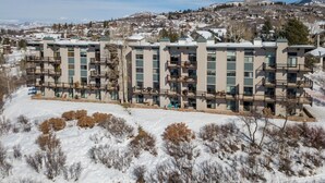 Un hotel de varios pisos con balcones, ubicado en una ladera nevada y con vistas a un pueblo al fondo.