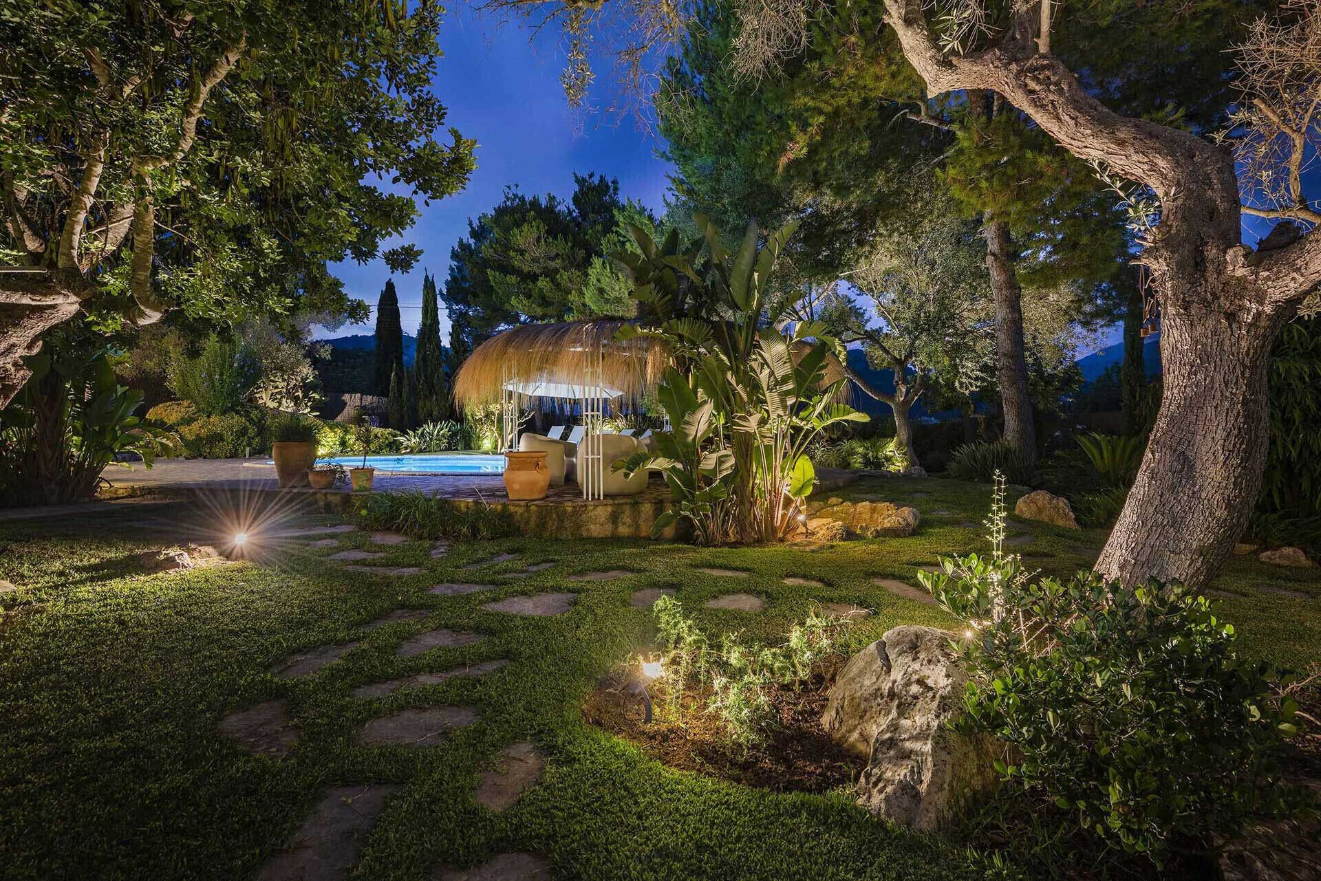 A well-lit outdoor area with a pool, lounge chairs, and a thatched structure.