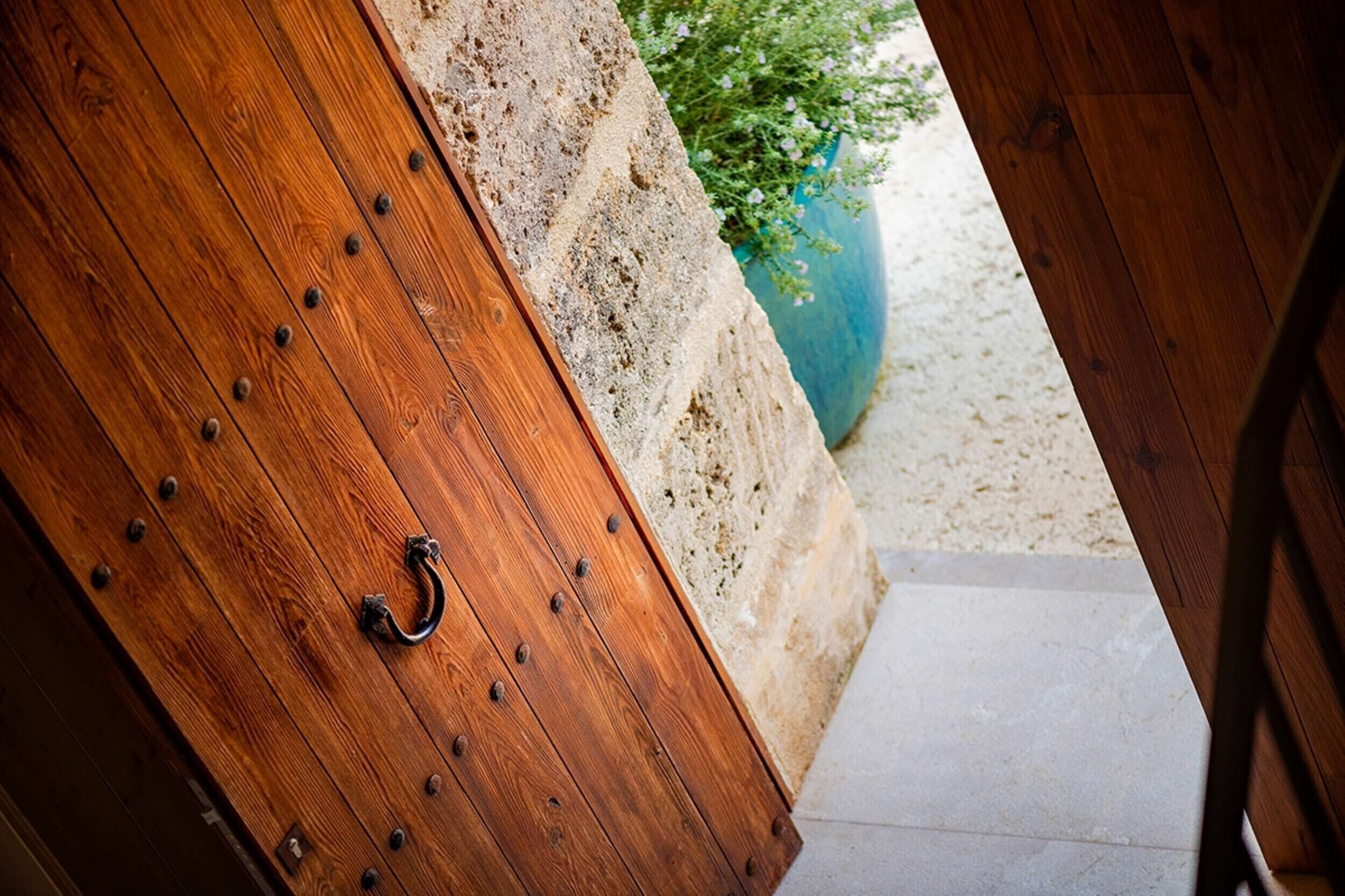 A wooden door with metal studs and a metal handle, leading to a stone wall and a potted plant.