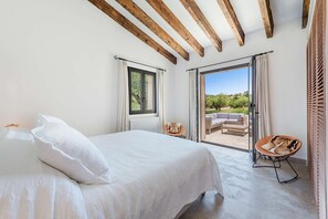 Ein Schlafzimmer mit einem großen Bett, Blick ins Freie und einer Terrasse mit Möbeln.