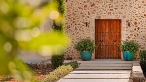 Un bâtiment en pierre doté d’une porte double en bois, de deux plantes en pot et d’un chemin de pierre menant à l’entrée.