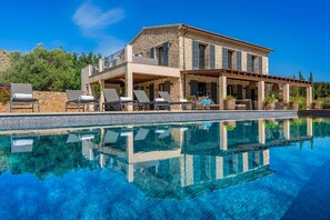 Ein zweistöckiges Steinhaus mit Pool, Außenbereich und überdachter Terrasse.