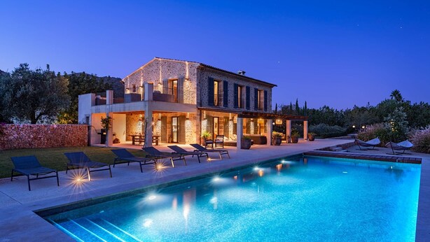Une maison moderne dotée d’une piscine, de chaises longues et d’un mur en pierre.
