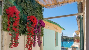 A balcony with a view of the sea, a table with a plate of food and drinks, and hanging flowers. - Dina house (Lakka)