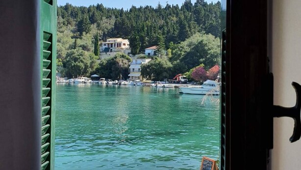 A view from a window overlooking a body of water with boats, a dock, and buildings on a hillside. - Dina house (Lakka)