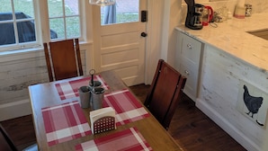 A cozy kitchen with a wooden table set for dining, a hanging light fixture, and a window with a view of the backyard. - The Flowers House - Downtown Historic Home in the Heart of Mount Dora (Mount Dora)