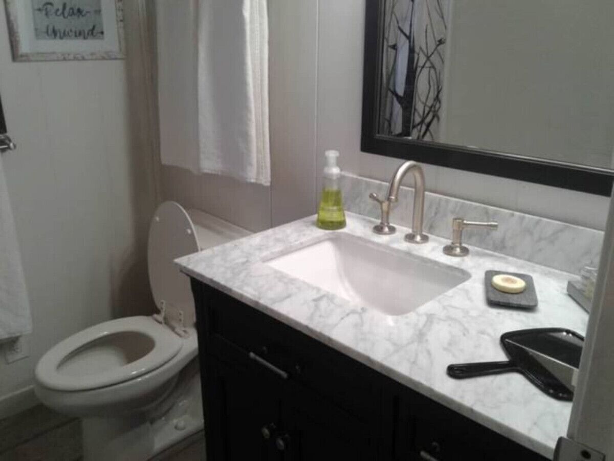 Un baño con inodoro blanco, lavamanos con espejo y dispensador de jabón.