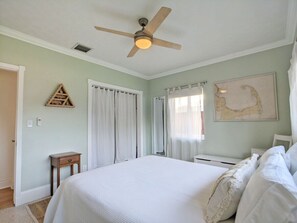 A bedroom with a large bed, a ceiling fan, a wooden nightstand, and a map on the wall.