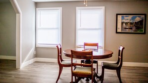 A dining area with a round table and four chairs, two windows with blinds, and a ceiling fan. - Holland Suites, Suite #4 (Williamstown)