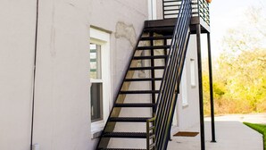 A building with a black metal staircase leading to a landing. There is a small table and a chair outside the building. - Holland Suites, Suite #4 (Williamstown)