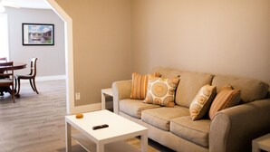 A living room with a beige sofa, patterned cushions, a white coffee table, and a framed picture on the wall. - Holland Suites, Suite #4 (Williamstown)